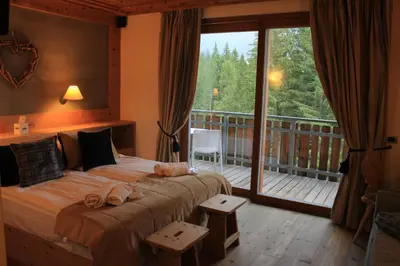 a bedroom with a bed and a balcony with a large window at Ciasa Vervei in Cortina dʼAmpezzo