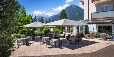 a patio with tables and chairs and white umbrellas at Hotel Ifinger in Schenna
