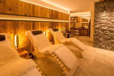 a room with four white couches and a stone wall at Apartments Antines in Selva di Val Gardena