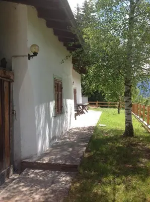 a white building with a tree next to a sidewalk at Baita cavalese giardino esclusivo in Cavalese