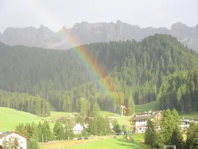 a rainbow over a green field with houses and trees at Appartamento Puez in Selva di Val Gardena