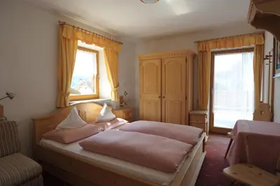 a bedroom with a bed with pink sheets and two windows at Pension Peintner in Gais