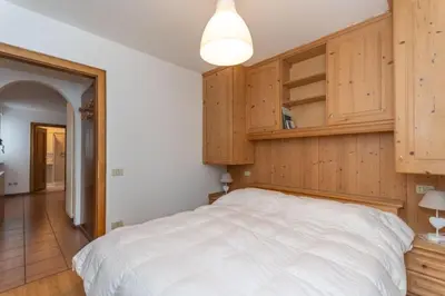 a bedroom with a white bed and wooden cabinets at Casa Alice in Falcade
