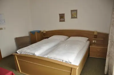 a bed with white sheets and a wooden headboard at Garni Kofler in Tirolo