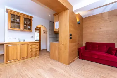 a living room with a red couch and a kitchen at Appartamento Vajolet in Pozza di Fassa