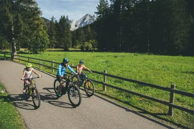 three people riding bikes on a path next to a fence at Appartamenti Césa Col De Pin in Canazei