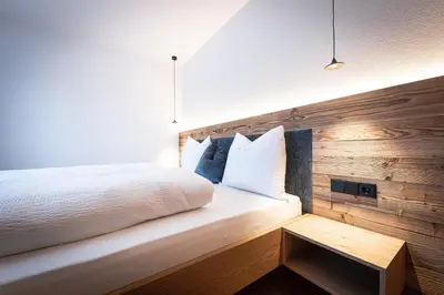 a bedroom with a white bed and a wooden wall at MANARES - my mountain stay in San Lorenzo di Sebato