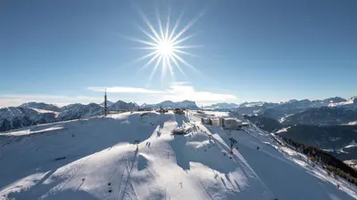 a snow covered ski slope with the sun in the sky at Kronplatz Mountain Lodge in Brunico