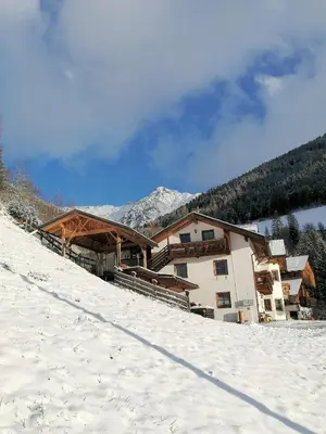 a building on a snow covered slope with mountains in the background at Wiesenheimhof - Apt 1 in Terento
