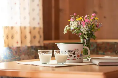 a table with a vase of flowers and a cup of milk at Schusterhof - Urlaub auf dem Bauernhof in Novale