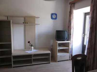 a room with a tv and a table with a vase of flowers at Gasthof zum Roessl in San Genesio Atesino