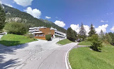 an empty road with a building on the side of a mountain at Casa Franz in Val di Fassa by Zoom In Earth in Mazzin