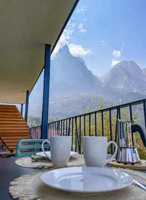 a table with two coffee cups on a balcony with mountains at Amontis Dolomites in Siusi