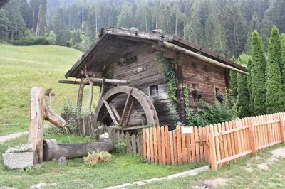 an old wooden house with a watermill next to a fence at Pension Gasthof Haselstaude in San Leonardo in Passiria