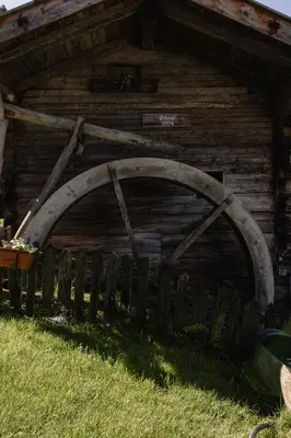 a wooden barn with a wooden wheel in the grass at Pension Gasthof Haselstaude in San Leonardo in Passiria