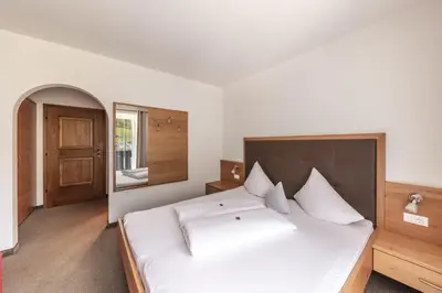 a bedroom with a large white bed with a wooden headboard at Pension Gasthof Haselstaude in San Leonardo in Passiria