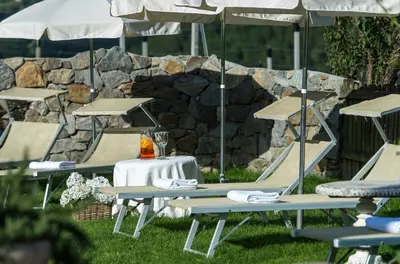 a group of picnic tables with umbrellas and a stone wall at Hotel Chalet Gravenstein in Tirolo