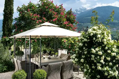 a table with an umbrella in a garden with flowers at Hotel Chalet Gravenstein in Tirolo