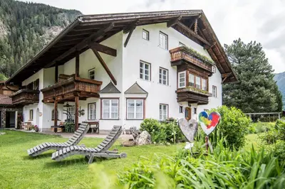 a large white house with two chairs in the yard at Rieplhof - Relaxing farm stay with breakfast and mountain view in Vipiteno