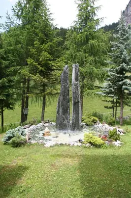 a fountain in the middle of a field with trees at Hotel Val in Selva di Val Gardena