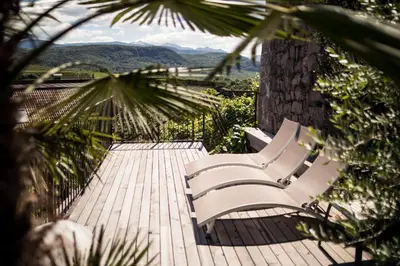 two white benches sitting on a wooden deck with a tree at Romantik Hotel Jagdhof in Caldaro