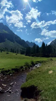a river in a field next to a field with mountains at Casa Micéi in Tesero