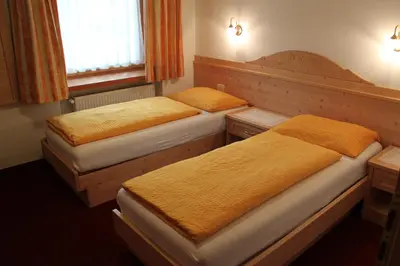 two beds in a small room with orange sheets at Garni Reutlingen in Colfosco