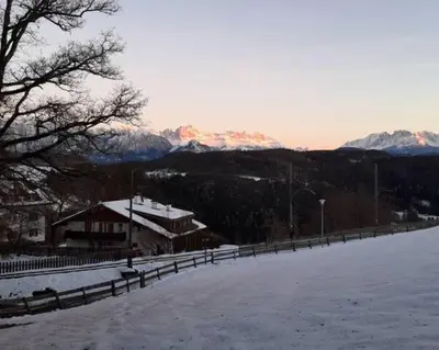 a snow covered field with a building and mountains at Apartment Lärchenheim in Soprabolzano
