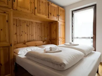 two beds in a bedroom with wooden walls and a window at Family Hut in Carano