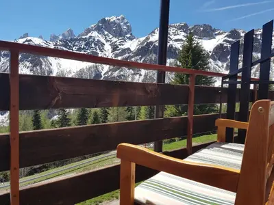 a chair on a balcony with a view of mountains at Casa Lares in Falcade