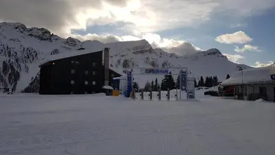 a building in the snow in front of a mountain at Casa Lares in Falcade