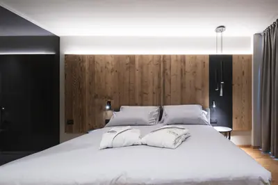 a bedroom with a large white bed with wooden walls at DOLOMITI EXCLUSIVE YOUR MOUNTAIN SUITE in Pozza di Fassa