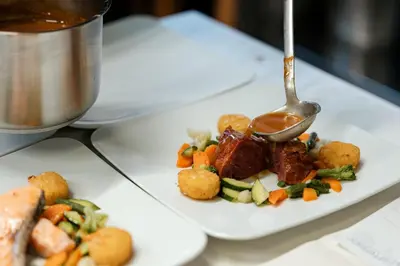 a plate of food with meat and vegetables with a spoon at Hotel Cristallo in Santa Cristina in Val Gardena