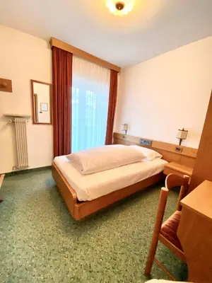 a bedroom with a bed and a desk and a window at Affittacamere Garden Cavalese in Cavalese