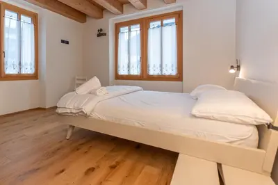 a bedroom with a bed with white sheets and windows at Villa Caterina in Falcade