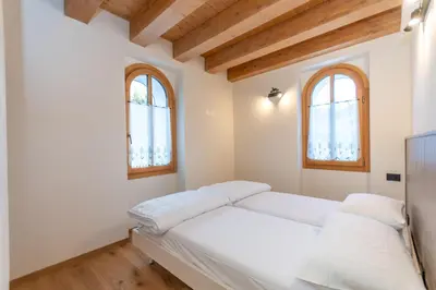 a bedroom with a white bed with two windows at Villa Caterina in Falcade
