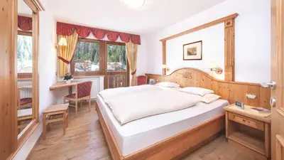 a bedroom with a bed and a desk and a window at Residence Carin in Selva di Val Gardena