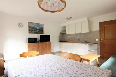 a bedroom with a white bed and a kitchen at Planhof Apartments in San Martino in Badia
