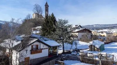 a village in the snow with a clock tower at Agritur Iellici in Castello di Fiemme