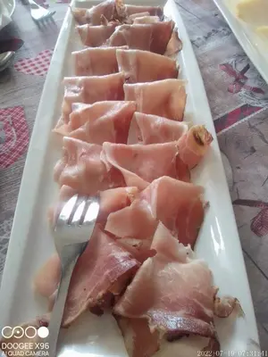 a white plate with ham and a fork on it at B&B SòT AL PIZ in Sagron Mis