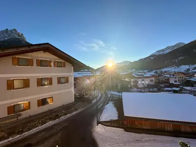 a building with the sun setting in the snow at Ciasa De Doni in Pozza di Fassa