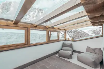 a room with a couch and windows with mountains at Hotel Piz Seteur in Selva di Val Gardena