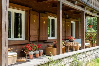 a porch with pots of flowers and tables and windows at B&B Villa La Bercia in San Vigilio Di Marebbe