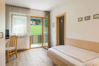 a bedroom with a bed and a desk and a window at B&B Garni Schorneck in Brunico