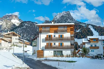 a building in the snow with mountains in the background at apartment allium in Selva di Val Gardena