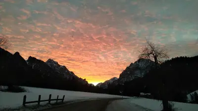 a sunset over a road in the mountains with snow at B&B Villa Dolomites Hut in San Vigilio Di Marebbe