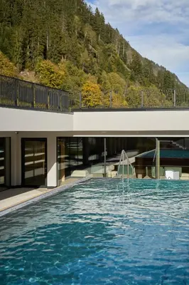 a swimming pool with a building with a mountain at Berghotel in Racines