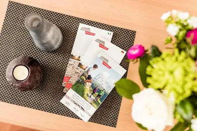 a table with a magazine and a candle and flowers at Appartamenti Hetty in Santa Cristina in Val Gardena