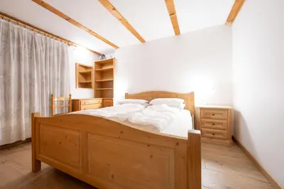 a bedroom with a wooden bed with white sheets at Cesa alla Cascata in Canazei