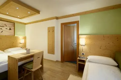 a room with two beds and a desk and a table at Residence Ciasa Morin in Corvara in Badia
